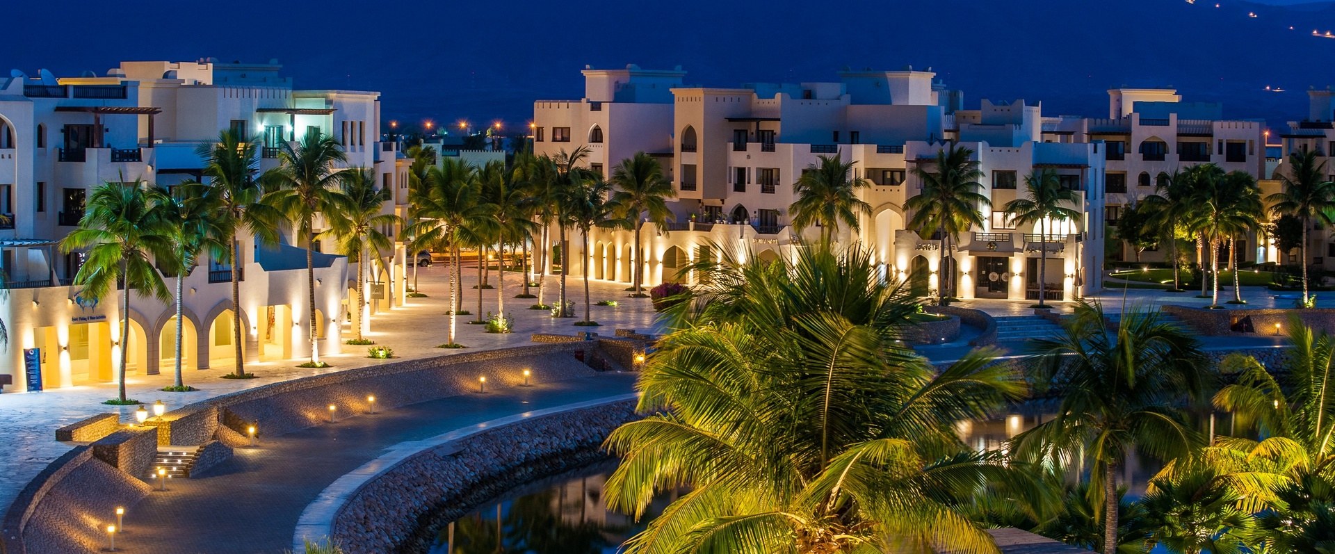 Hawana Salalah — marina and resort buildings at dusk with mountains behind